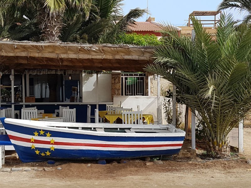Wooden boat painted like the Cape Verdean flag in front of a beach restaurant
